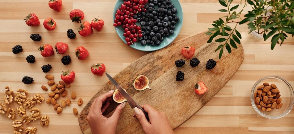Overhead shot of fresh fruits, nuts, and hands preparing ingredients on a wooden board.