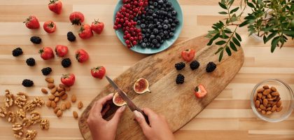 Overhead shot of fresh fruits, nuts, and hands preparing ingredients on a wooden board.