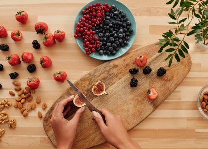 Overhead shot of fresh fruits, nuts, and hands preparing ingredients on a wooden board.