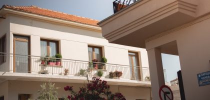 Traditional Greek house facade with potted plants and balcony details.